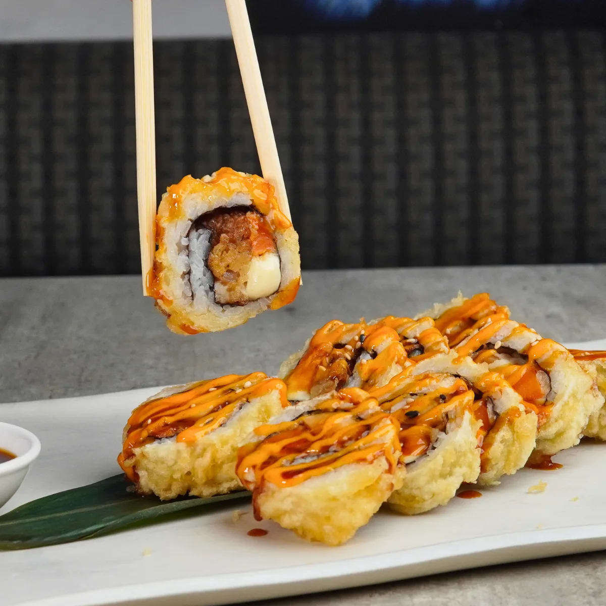 A Chicken Crazy roll, deep fried and sauced with teriyaki and spicy mayo, one piece lifted on chopsticks