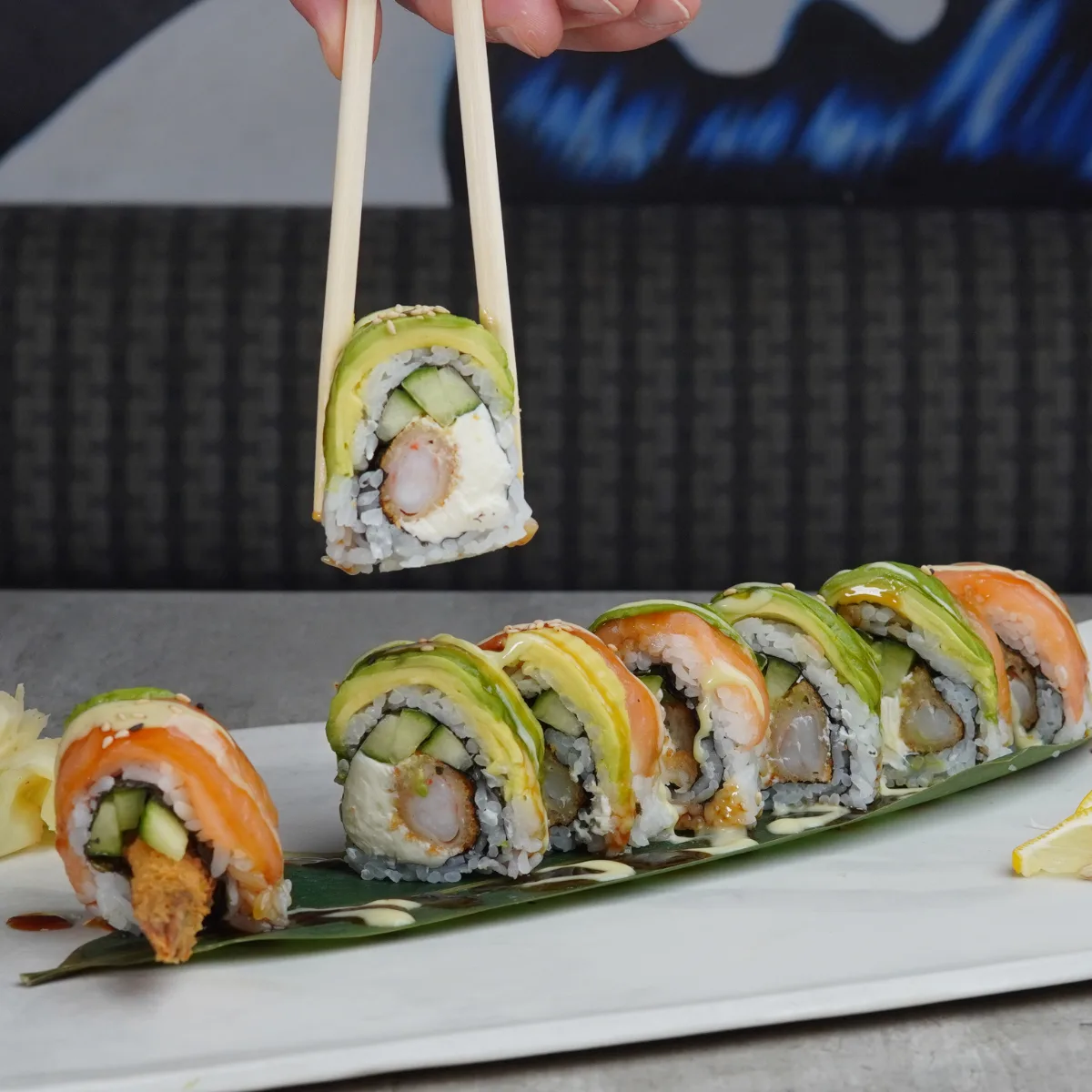A Golden Boy roll topped with fresh salmon and avocado, one piece lifted on chopsticks