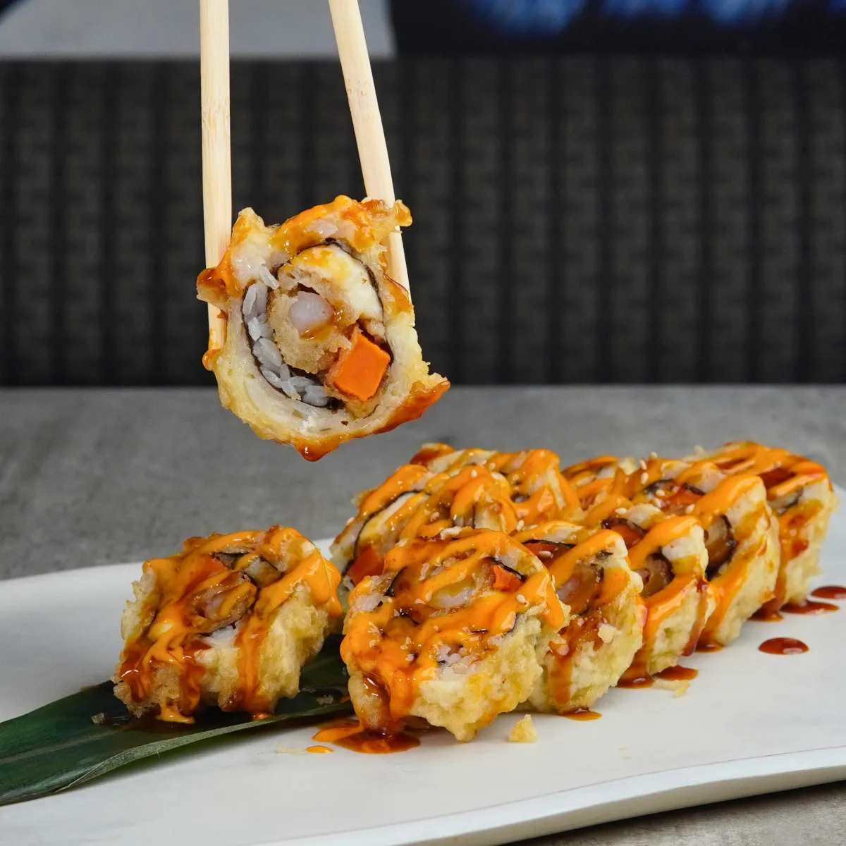 A Shrimp Crazy roll on a banana leaf, one piece lifted on chopsticks