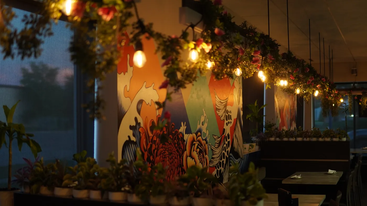 A painted mural of waves and flowers under hanging greenery and string lights